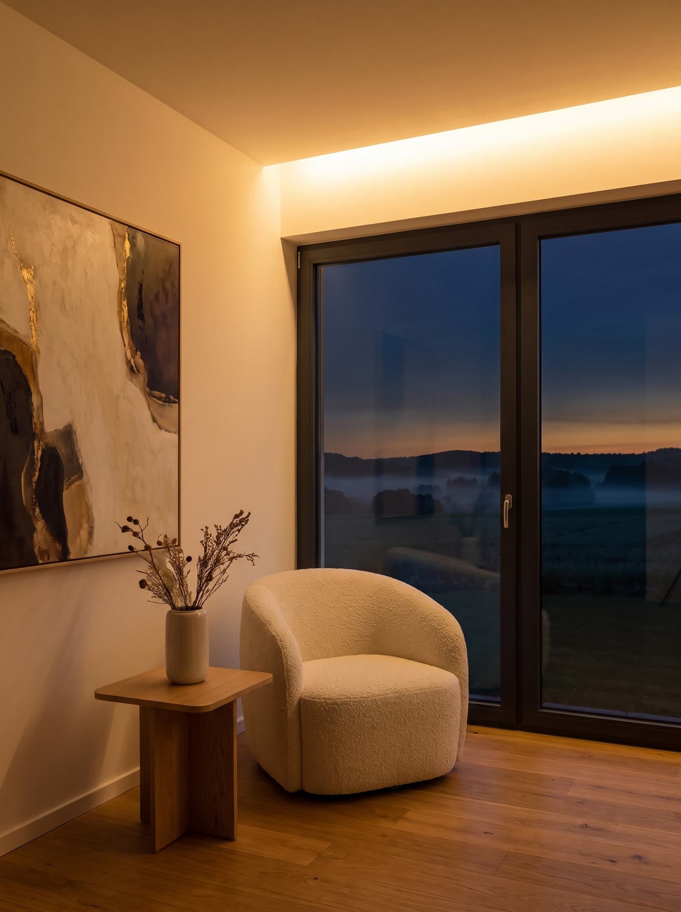 Warmer Wohnraum der Villa mit Boucle-Sessel, Kunstwerk und Blick in die Abenddämmerung